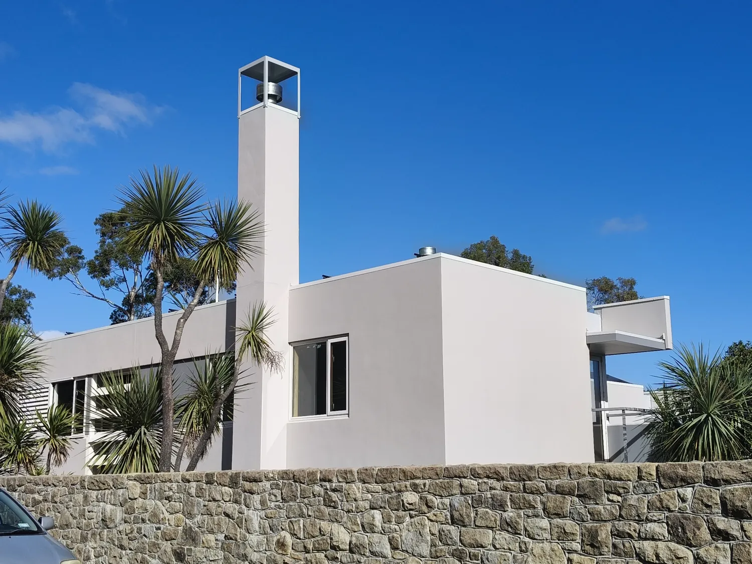 Modern flat-roof render home with tall plastered chimney above a stone wall