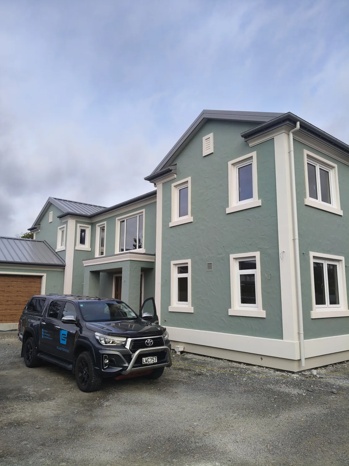 Two-storey home with sage green plaster finish and white window surrounds