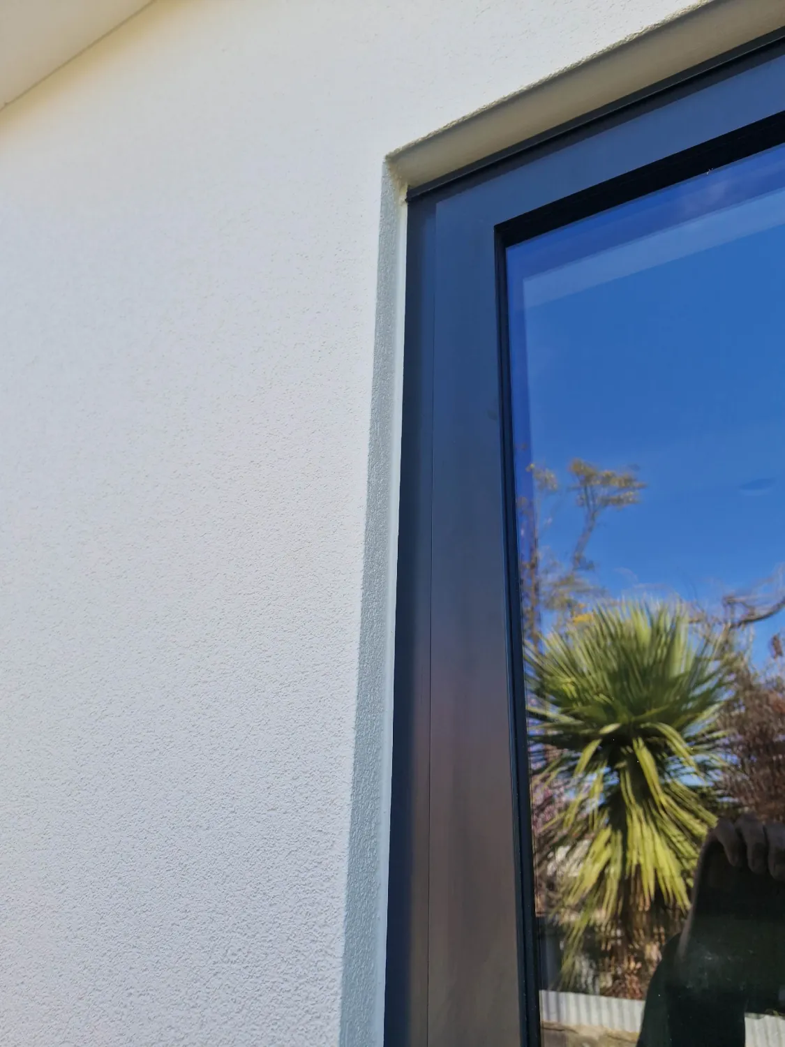 Close-up of textured white render meeting a dark-framed window